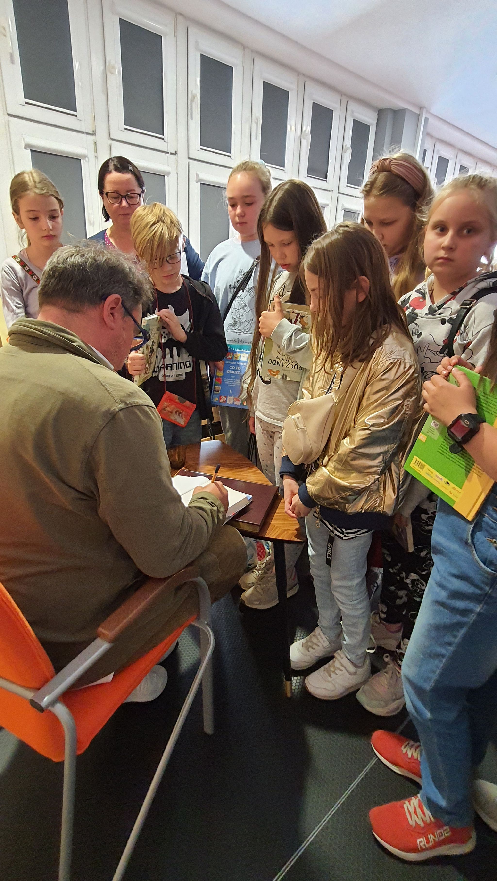 Grupa dzieci podczas spotkania z autorem książek czaka na podpis