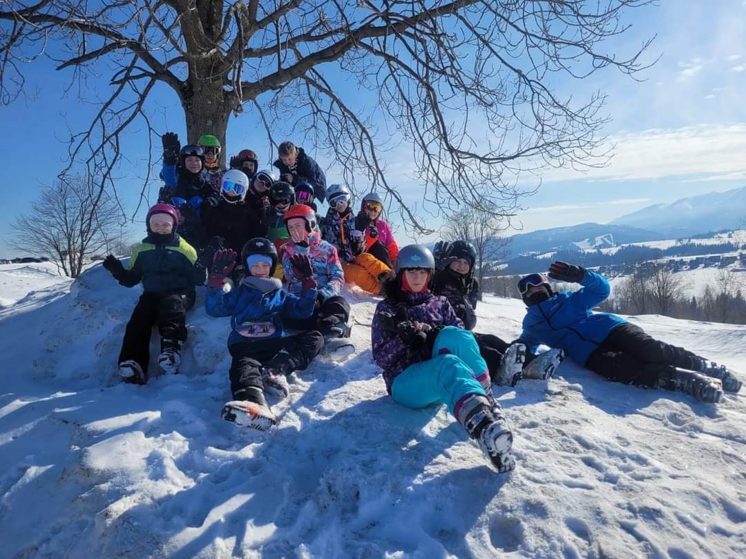 Grupa dzieci siedzi na śniegu pod drzewem
