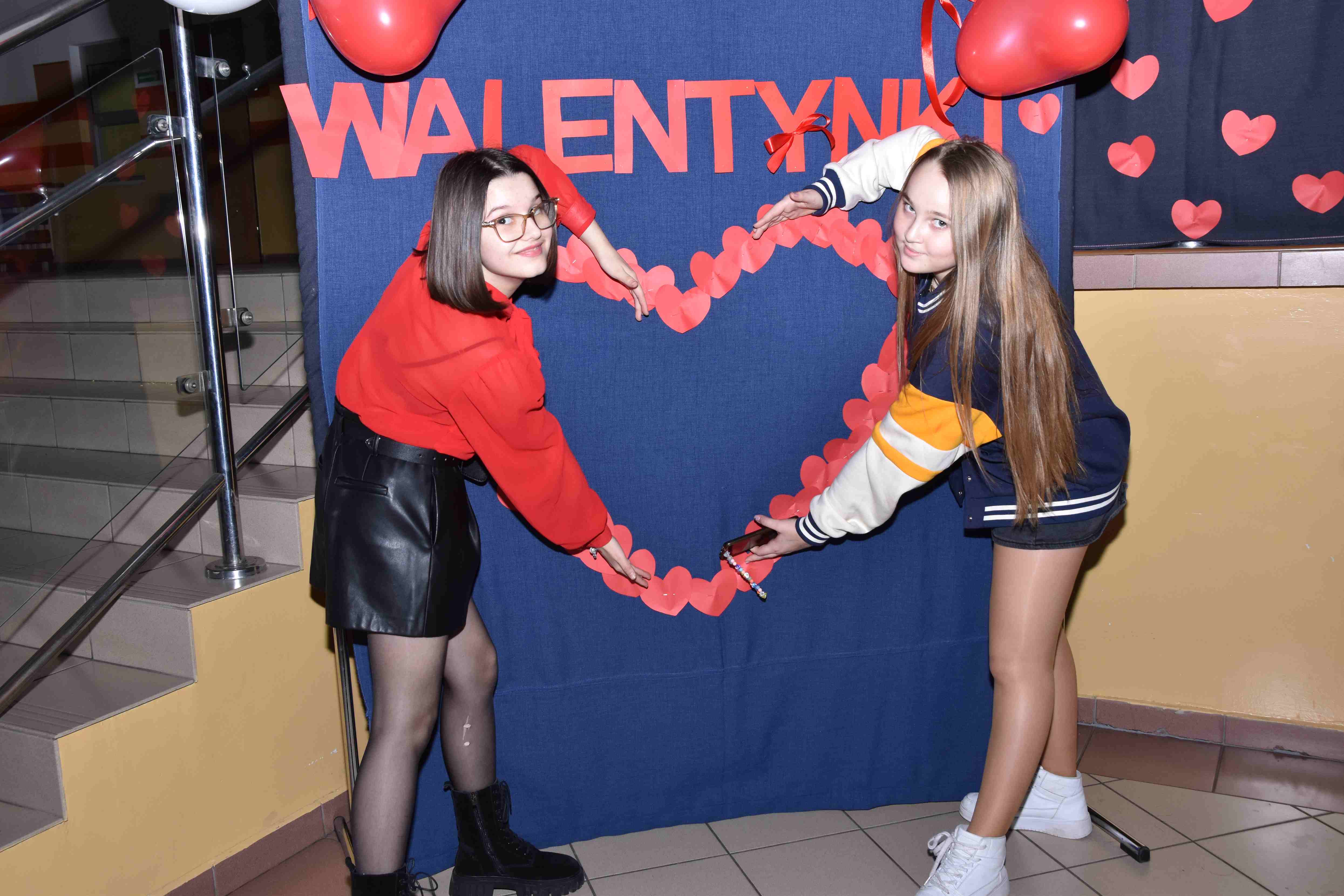 Dwie dziewczynki tworzą serce ze swoich rąk przed plakatem walentynkowym