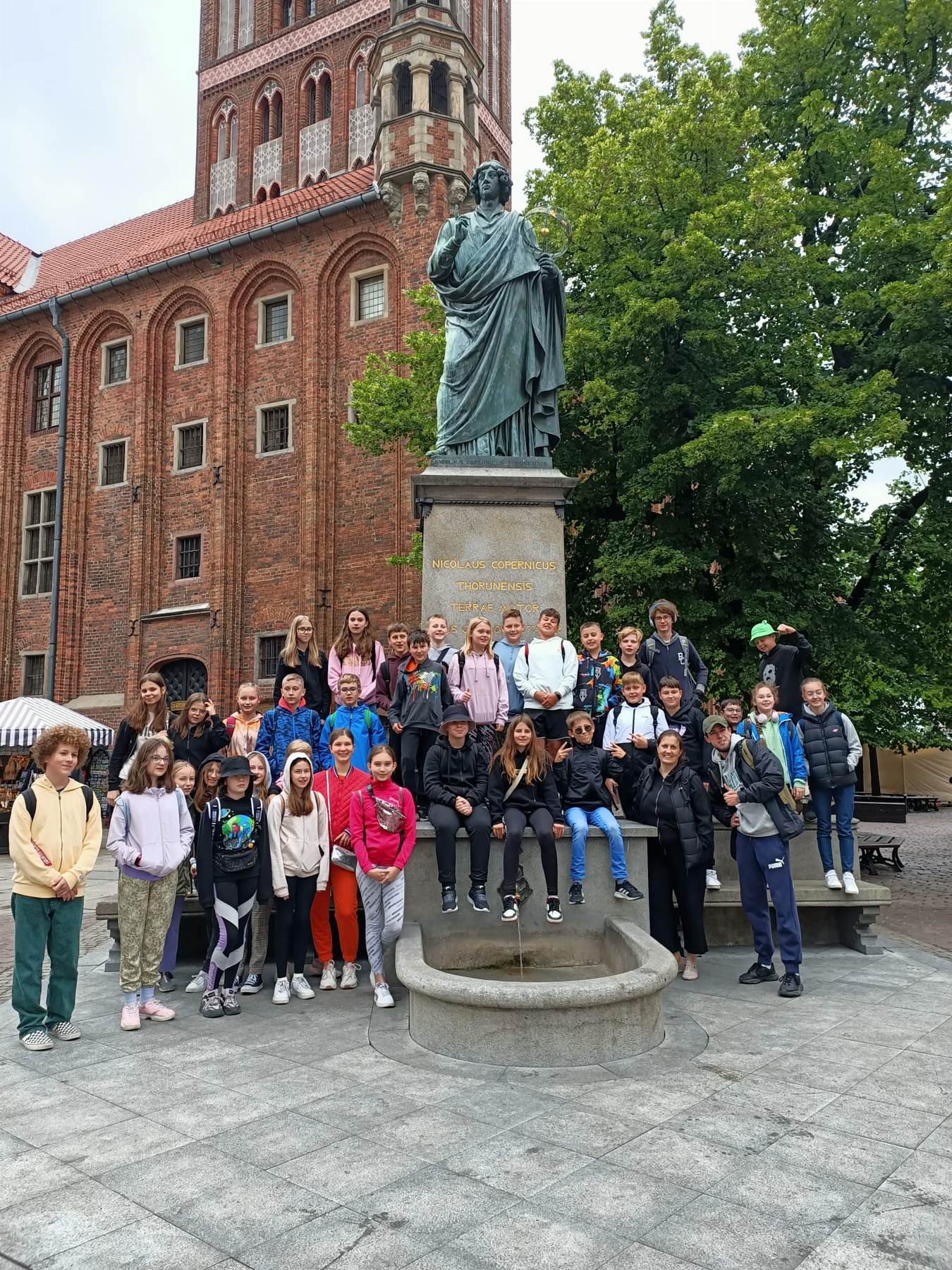 Grupa dzieci stoi przy pomniku Kopernika