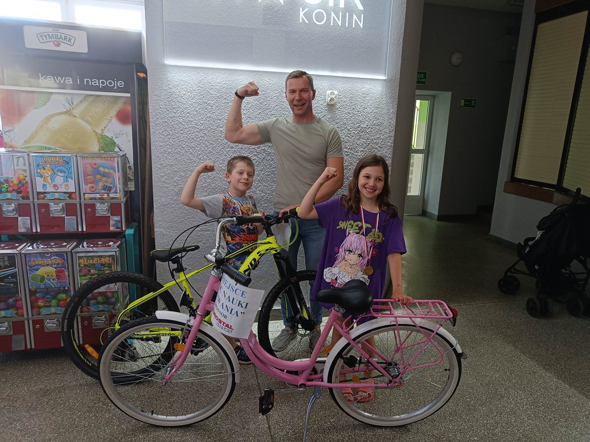 Dwoje dzieci pozuje do zdjęcia z trenerem i rowerami - nagrodami