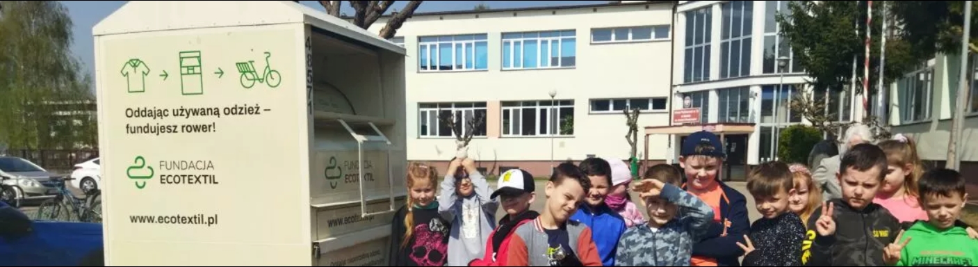 Grupa dzieci stoi przed szkołą przy kontenerze na ubrania